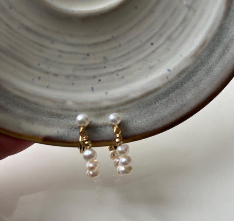 May include: A pair of gold clip-on earrings with a cluster of white pearls dangling from each.