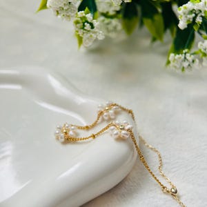 May include: A delicate gold chain necklace with small pearl flower accents. The necklace is on a white surface.