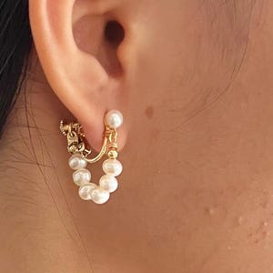 May include: Gold hoop earrings with a chain detail and a row of white pearls hanging from the bottom.