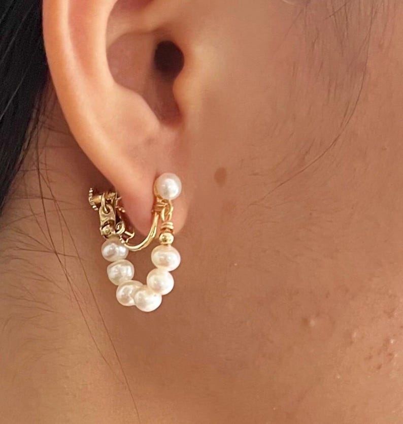 May include: Gold hoop earrings with a chain detail and a row of white pearls hanging from the bottom.