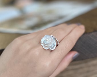 May include: A white pearl flower ring with a delicate silver band. The ring is set with a single pearl in the center of the flower.