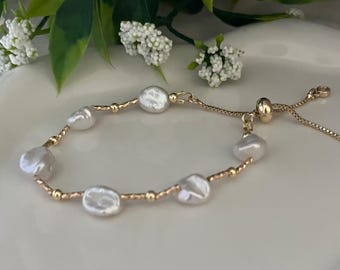 May include: A gold bracelet with six white, irregularly shaped pearls. Small gold beads and a delicate gold chain connect the pearls. The bracelet has an adjustable clasp. The pearls are a beautiful off-white colour.