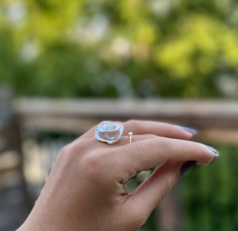 May include: A silver ring with a large, irregular, white pearl-like stone. The ring is on a person's finger.
