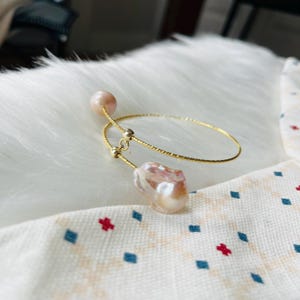 Peut inclure: Un bracelet jonc en or avec deux perles roses. Le bracelet est ouvert et pr&eacute;sente un design d&eacute;licat et textur&eacute;.