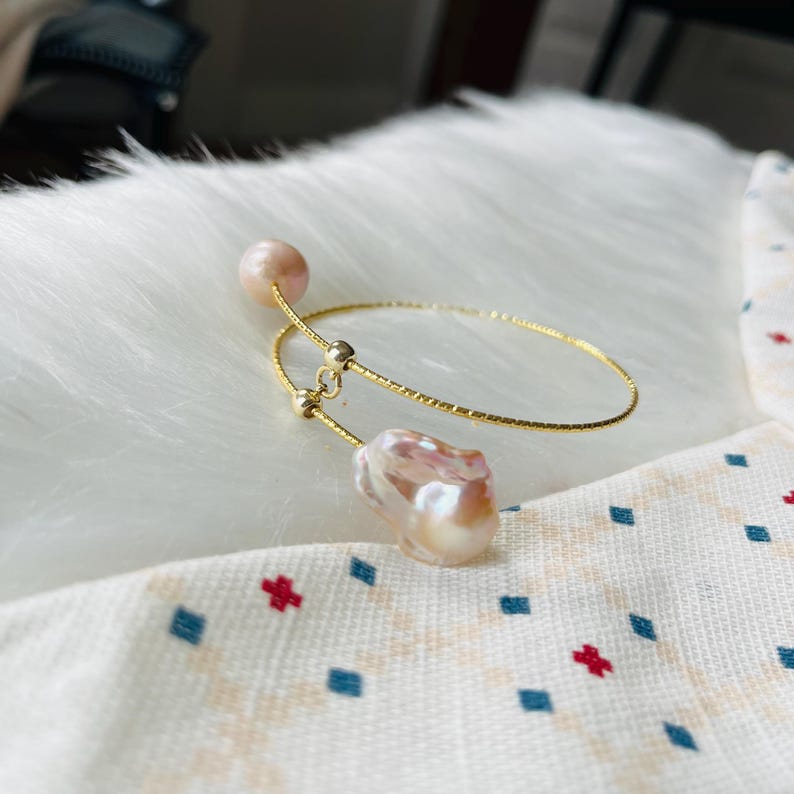 Peut inclure: Un bracelet jonc en or avec deux perles roses. Le bracelet est ouvert et pr&eacute;sente un design d&eacute;licat et textur&eacute;.