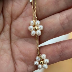May include: A delicate gold chain necklace with two pearl flower charms. Each flower charm is made of small white pearls arranged in a circular pattern.