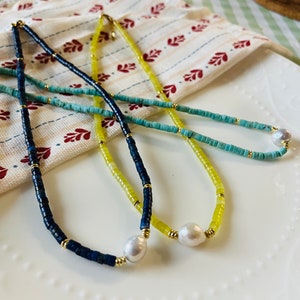 May include: Three necklaces with different colored beads and a pearl pendant. The necklaces are blue, yellow, and turquoise.