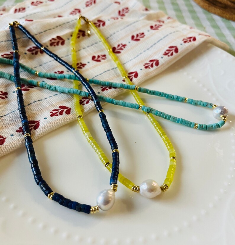 May include: Three necklaces with different colored beads and a pearl pendant. The necklaces are blue, yellow, and turquoise.