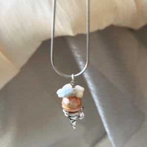 Peut inclure: Un collier en cha&icirc;ne argent avec un pendentif en forme de cornet de glace blanc et perle. Le pendentif a un petit strass bleu sur le c&ocirc;t&eacute;.
