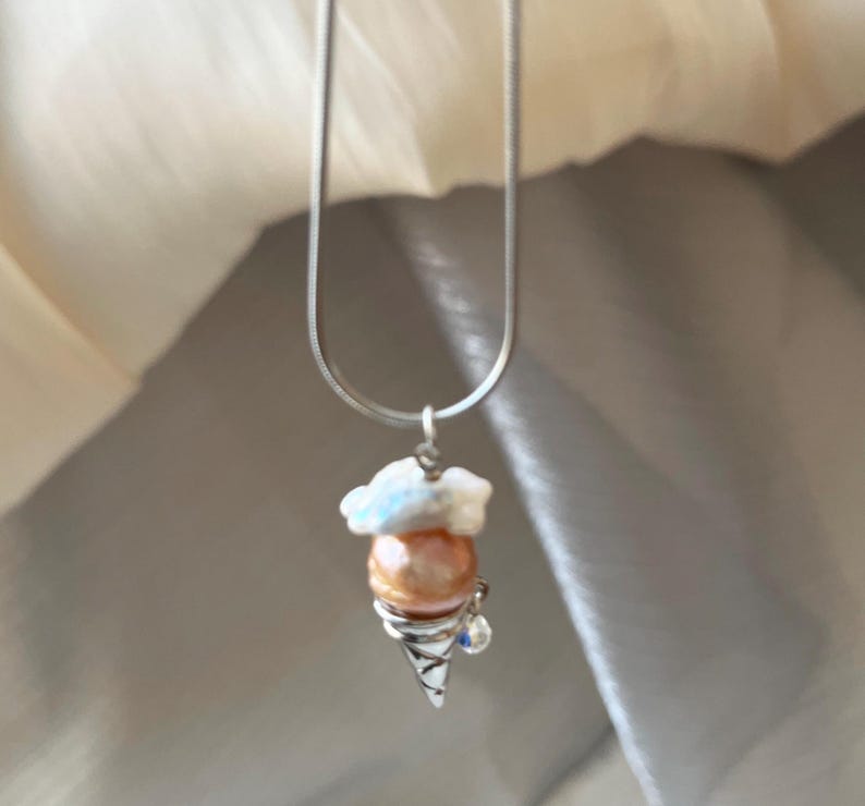 Peut inclure: Un collier en cha&icirc;ne argent avec un pendentif en forme de cornet de glace blanc et perle. Le pendentif a un petit strass bleu sur le c&ocirc;t&eacute;.