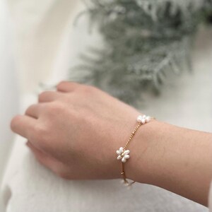 May include: A delicate gold chain bracelet with small white pearl flower accents.