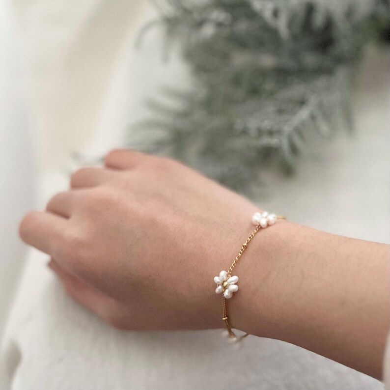 May include: A delicate gold chain bracelet with small white pearl flower accents.