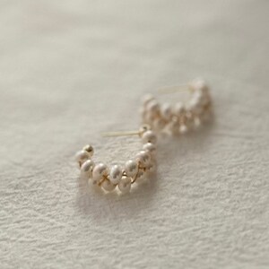 May include: A pair of gold hoop earrings with a delicate design of white pearls. The pearls are arranged in a staggered pattern, creating a unique and elegant look.