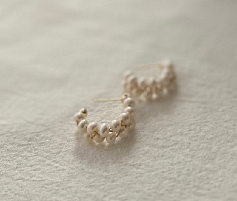 May include: A pair of gold hoop earrings with a delicate design of white pearls. The pearls are arranged in a staggered pattern, creating a unique and elegant look.