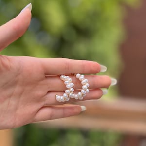 May include: A pair of gold hoop earrings with white pearl accents. The earrings are made of small, round pearls that are strung together in a continuous loop.