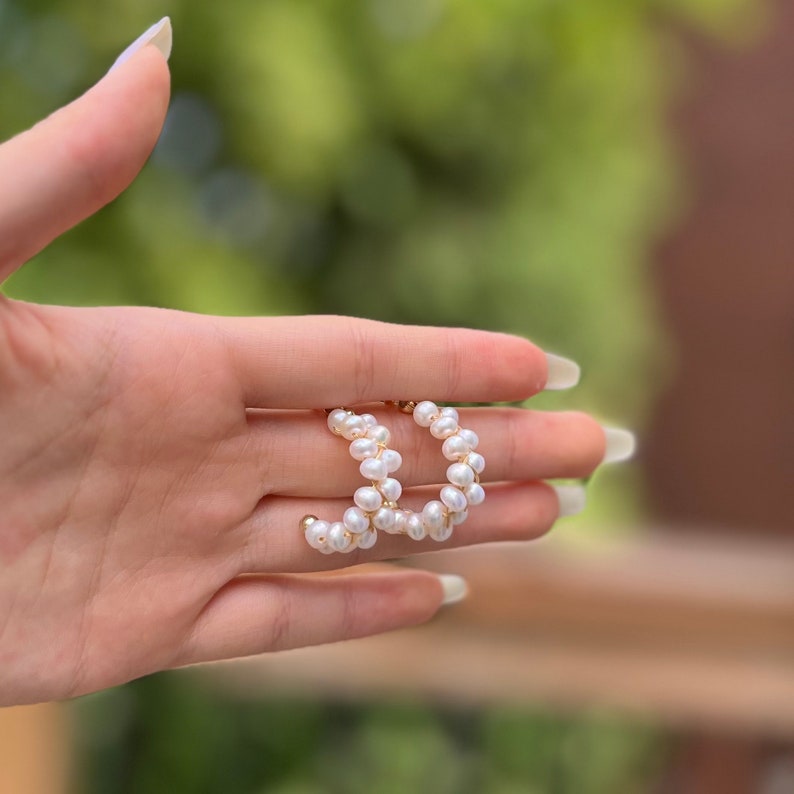 May include: A pair of gold hoop earrings with white pearl accents. The earrings are made of small, round pearls that are strung together in a continuous loop.