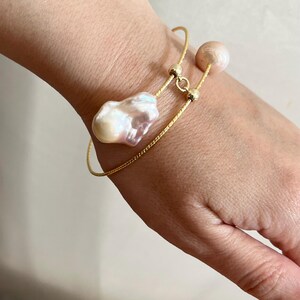 Peut inclure: Un bracelet en cha&icirc;ne dor&eacute;e avec deux accents de perles. La plus grosse perle est une perle baroque de forme irr&eacute;guli&egrave;re. La plus petite perle est ronde.