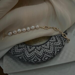 Puede incluir: Un brazalete de cadena dorada con cierre de palanca y una fila de perlas grandes y blancas.