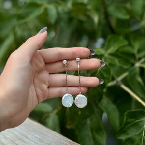 May include: A pair of long, delicate gold chain earrings with a white pearl at the top and a larger, round, white pearl at the bottom.
