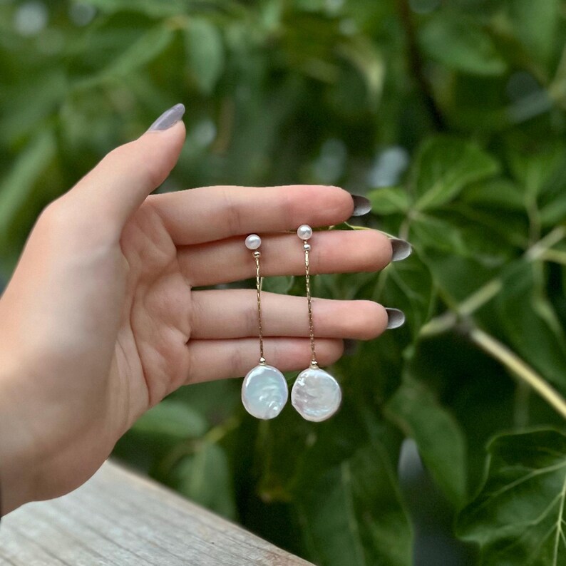 May include: A pair of long, delicate gold chain earrings with a white pearl at the top and a larger, round, white pearl at the bottom.