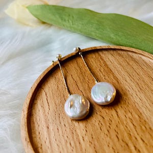 May include: A pair of gold dangle earrings with white pearl drops. The pearls are round and have a slight iridescent sheen.