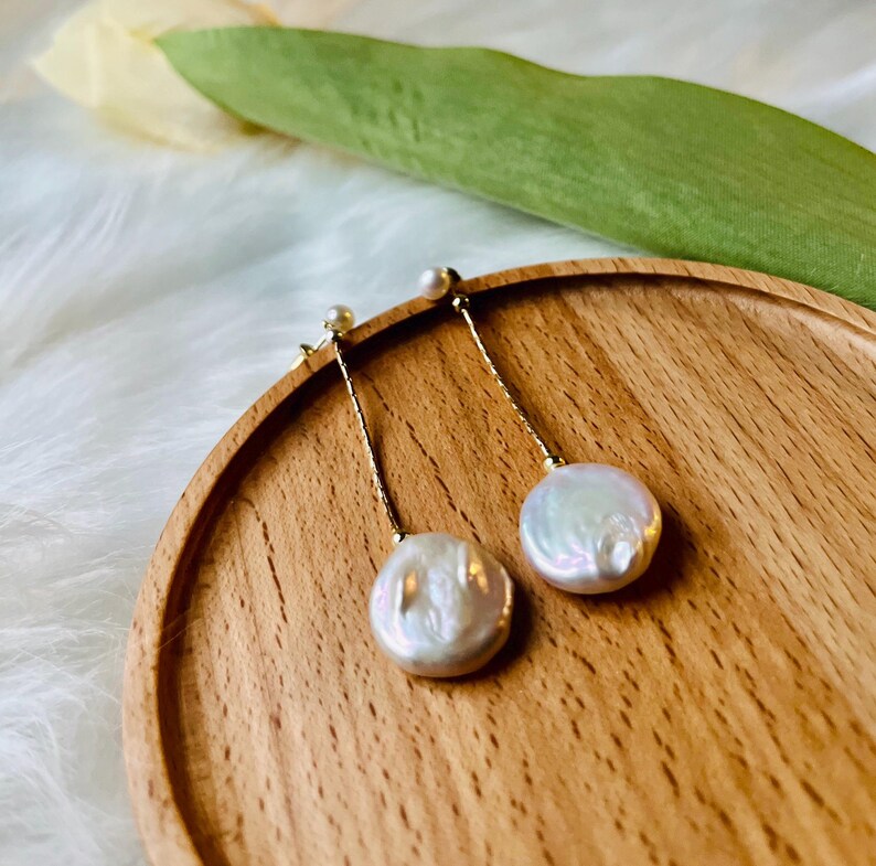 May include: A pair of gold dangle earrings with white pearl drops. The pearls are round and have a slight iridescent sheen.