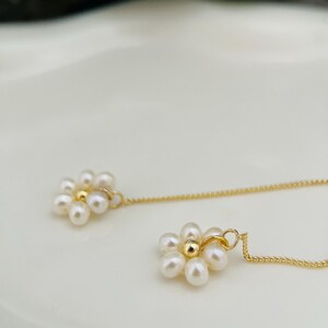 May include: A pair of gold chain earrings with pearl flower charms. Each charm features a cluster of small white pearls arranged in a flower shape with a gold bead in the center.
