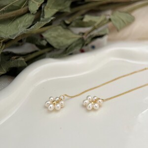 May include: A pair of gold chain earrings with small white pearl flower accents.