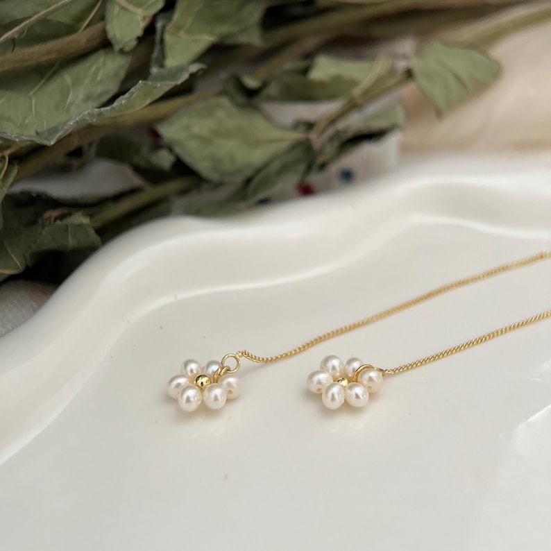 May include: A pair of gold chain earrings with small white pearl flower accents.