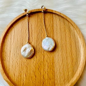 May include: A pair of gold dangle earrings with white pearl drops. The pearls are round and have an iridescent sheen.