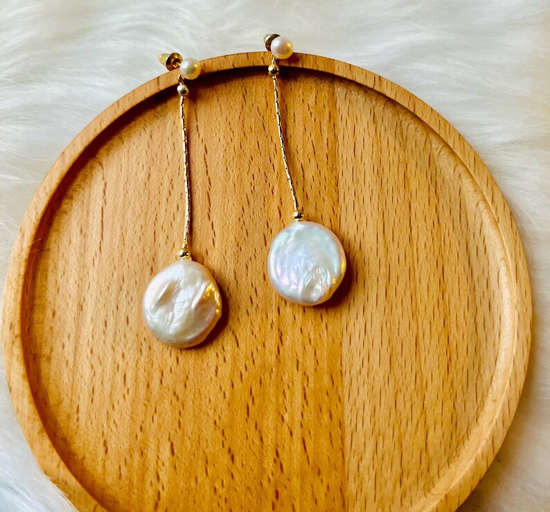 May include: A pair of gold dangle earrings with white pearl drops. The pearls are round and have an iridescent sheen.