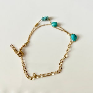 May include: A gold chain bracelet with turquoise stones and beads. The bracelet has a lobster clasp closure.