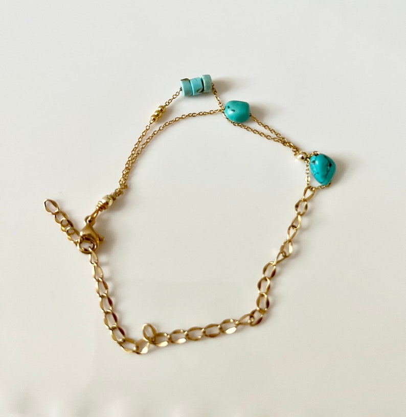 May include: A gold chain bracelet with turquoise stones and beads. The bracelet has a lobster clasp closure.
