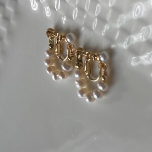 May include: A pair of gold-toned clip-on earrings with a pearl design. The earrings are made of small, white pearls arranged in a circular shape.