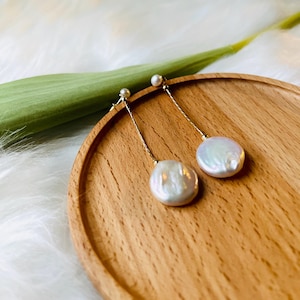 May include: A pair of gold dangle earrings with white pearl drops. The pearls are oval shaped and have a slight iridescent sheen.