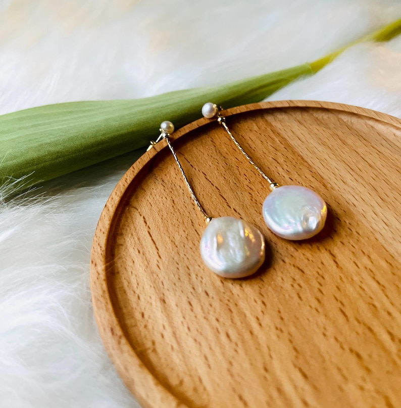 May include: A pair of gold dangle earrings with white pearl drops. The pearls are oval shaped and have a slight iridescent sheen.