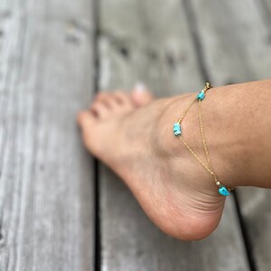 May include: A gold chain anklet with turquoise beads. The anklet is on a person's ankle.