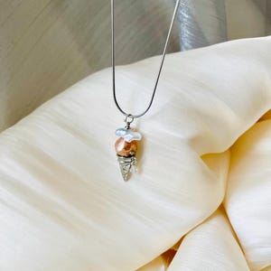 Peut inclure: Un collier en cha&icirc;ne argent avec un pendentif en forme de cornet de glace. La glace est faite d'une perle rose et blanche.