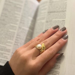 May include: A gold ring with a large white pearl set in a twisted band.