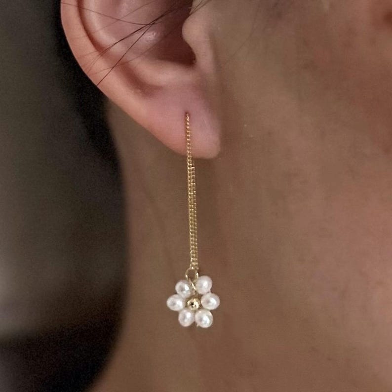 May include: Gold chain earrings with a pearl flower charm. The earrings are long and dangle from the earlobe.