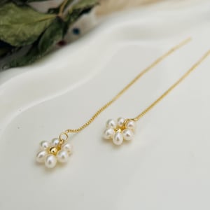May include: A pair of gold chain earrings with a small cluster of white pearls in the shape of a flower at the end of each chain.