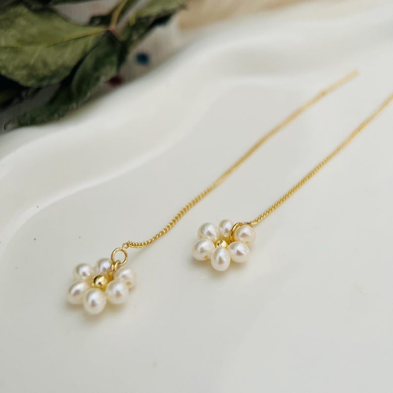 May include: A pair of gold chain earrings with a small cluster of white pearls in the shape of a flower at the end of each chain.