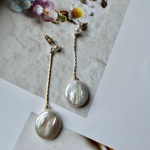 May include: A pair of gold dangle earrings with a large white pearl and a smaller pearl at the top of the chain.