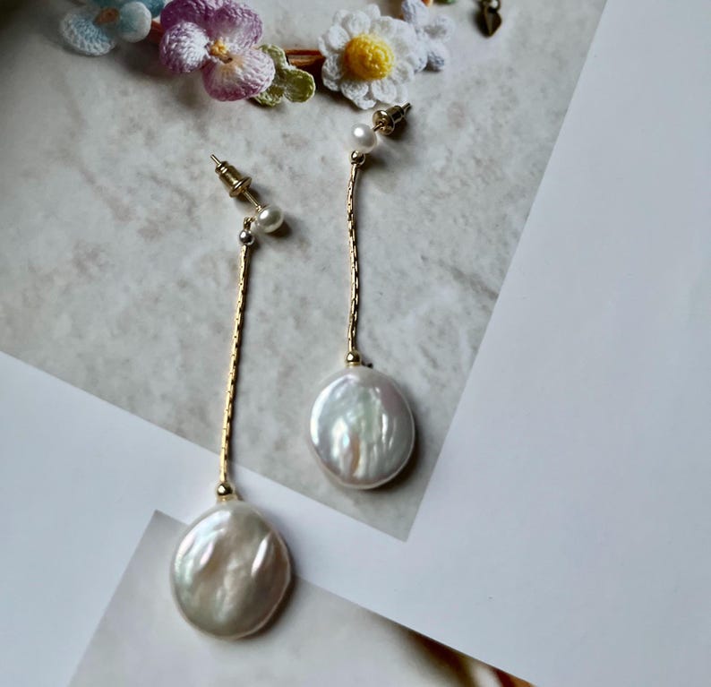May include: A pair of gold dangle earrings with a large white pearl and a smaller pearl at the top of the chain.