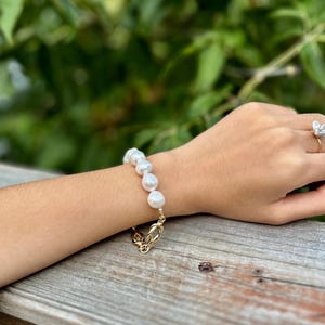 Puede incluir: Un brazalete de cadena dorada con una serie de grandes perlas blancas.