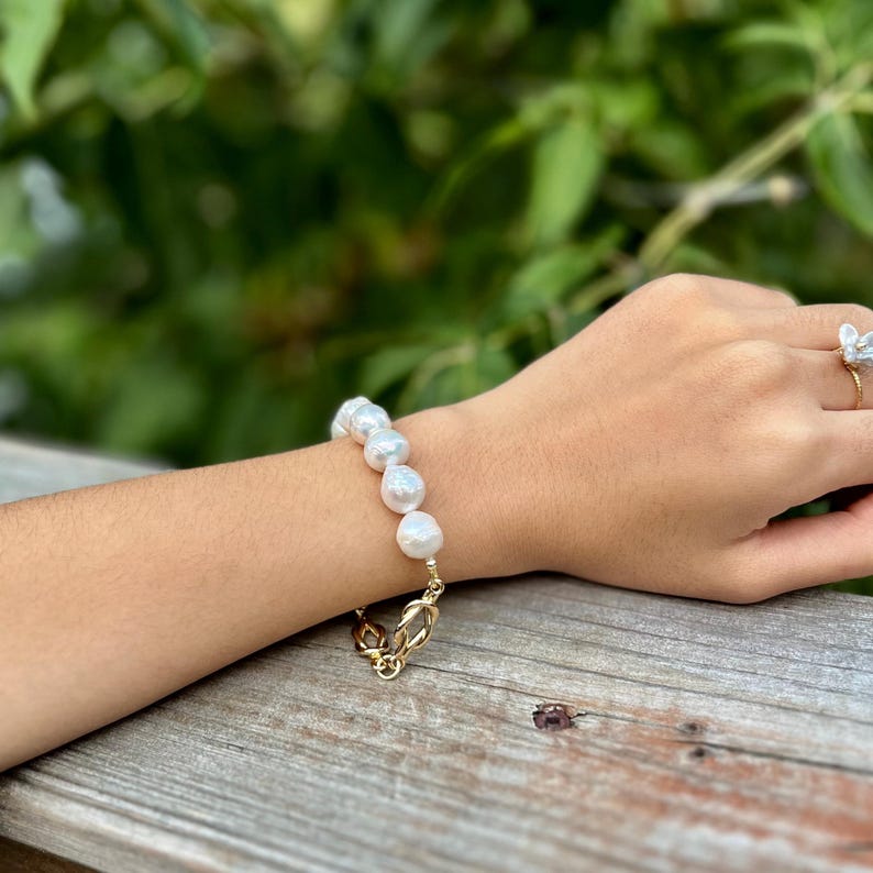 Puede incluir: Un brazalete de cadena dorada con una serie de grandes perlas blancas.