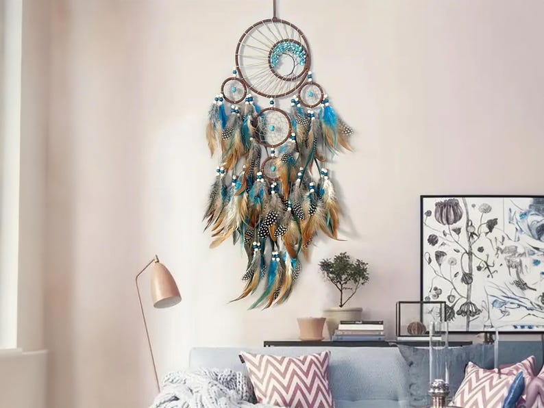 K&ouml;nnte beinhalten: Ein gro&szlig;er Traumf&auml;nger mit braunen und blauen Perlen und Federn. Der Traumf&auml;nger hat ein kreisf&ouml;rmiges Design mit einem netzartigen Muster und h&auml;ngt an einer wei&szlig;en Wand.