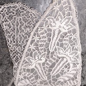以下が含まれることがあります： オフホワイトのレースアップリケ。詳細な花と葉の模様が施された三角形のセクションと、複雑に絡み合う糸のデザインが特徴的な曲線状のセクションで構成されており、繊細な針仕事が施されています。
