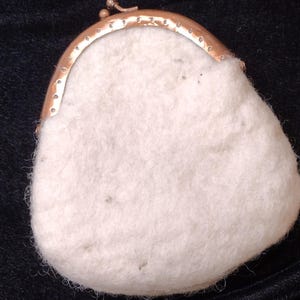 May include: A small, off-white felted coin purse with a textured, fuzzy surface and a metallic rose gold-toned kiss-lock frame. The pouch has a rounded, irregular shape and features a secure metal clasp closure at the top.