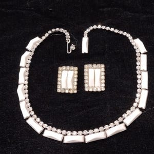 May include: A jewelry set consisting of a necklace and a pair of rectangular earrings. The necklace features alternating clear round rhinestones and white rectangular stones. The earrings match, with a central white stone bordered by clear rhinestones.